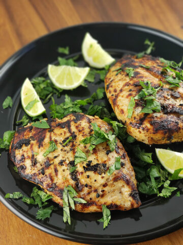 Grilled chicken breasts topped with cilantro and served with lime wedges