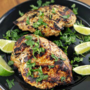 Grilled chicken breasts with cilantro and lime wedges on a black plate