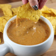 Hand dipping a tortilla chip into cheesy queso dip