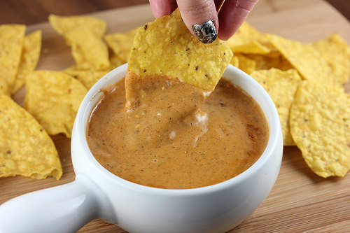 Hand dipping a tortilla chip into cheesy queso dip