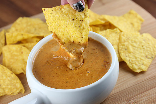 Chip dipped into creamy queso in a white bowl