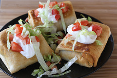 Plated chimichangas topped with lettuce, tomatoes, and sour cream