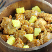Pineapple chicken pieces in a wooden bowl over rice