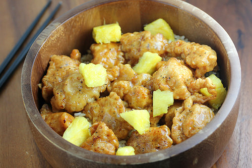 Pineapple chicken pieces in a wooden bowl over rice