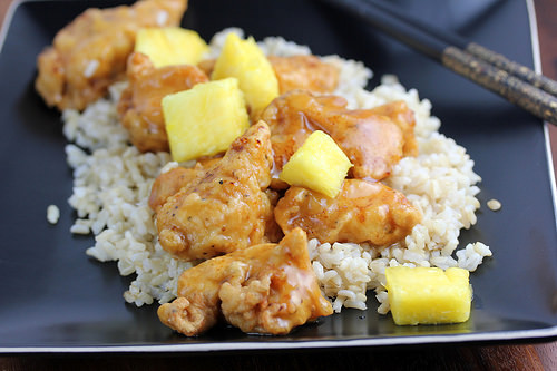 Pineapple chicken served over rice in a black plate