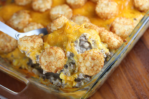 Spoonful of cheesy tater tot casserole being lifted from the dish