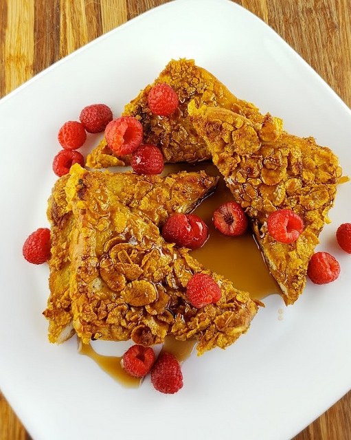 Crunchy French toast plated with raspberries and maple syrup