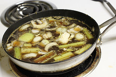 Skillet with broth, onions, and vegetables for French dip