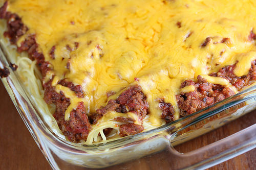 Baked spaghetti casserole topped with melted cheddar cheese