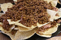 Ground beef layered over tortilla chips in a skillet