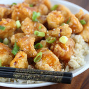 Sriracha chicken pieces on rice topped with green onions and chopsticks beside the bowl