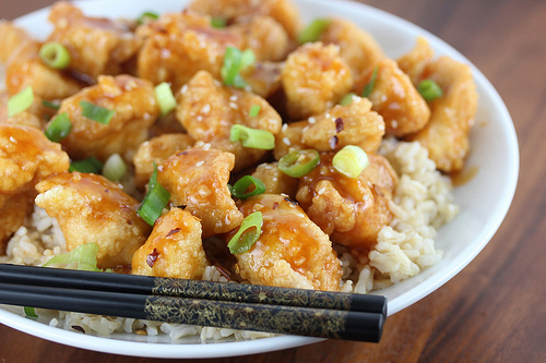 Sriracha chicken pieces on rice topped with green onions and chopsticks beside the bowl