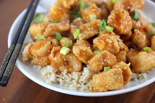 Crispy sriracha chicken served over rice in a white bowl with chopsticks