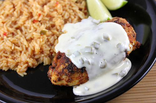 Close-up of the plated chicken topped with creamy queso beside rice