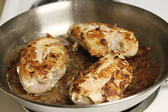 Seasoned chicken breasts cooking in pan