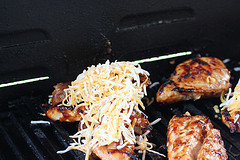 Grilled chicken topped with melted cheese on grill