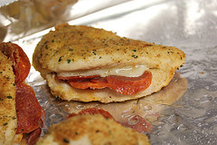 Breaded pepperoni stuffed chicken breast on baking sheet