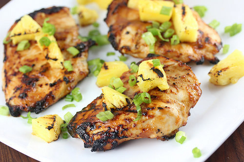 Grilled chicken with charred pineapple pieces on a white plate