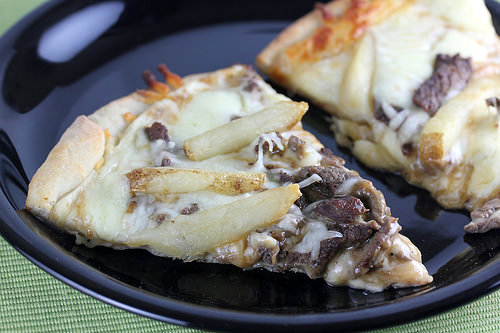 Slice of poutine pizza with beef gravy fries and melted cheese