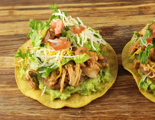 Chicken tostada with guacamole, shredded cheese, lettuce, and fresh tomato salsa