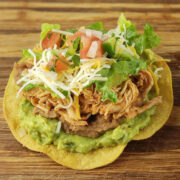 Shredded chicken tostada topped with guacamole, lettuce, cheese, and tomatoes