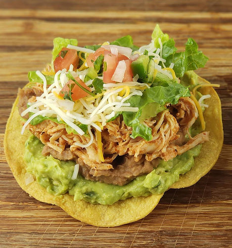 Shredded chicken tostada topped with guacamole, lettuce, cheese, and tomatoes