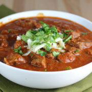 Slow cooker steak chili in a white bowl garnished with herbs and cheese