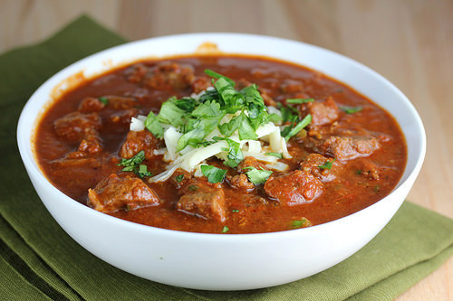 Slow cooker steak chili in a white bowl garnished with herbs and cheese